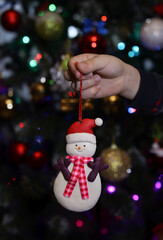  A cute snowman Christmas ornament surrounded by sparkling baubles and colorful holiday lights.