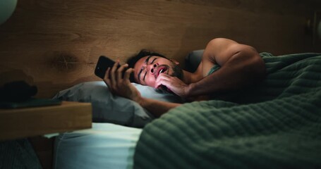 Late, tired man and yawn in bedroom with phone for social media, entertainment or online fatigue. Night, exhausted person and scroll in apartment with tech for mobile app, text message and sleepless.