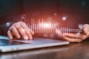 Person uses smartphone while sitting at desk with laptop and digital icons in the background