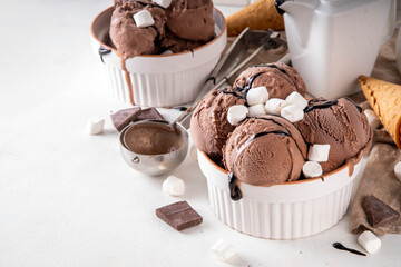 Hot chocolate ice cream with dark chocolate sauce and marshmallow. Gourmet rich chocolate gelato in white bowl, with drizzle of chocolate topping, on white kitchen table copy space