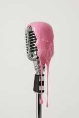 A classic chrome studio microphone, exuding a nostalgic retro charm, is unexpectedly adorned with vibrant pink liquid artfully dripping down its metallic grille and stand. This striking image is set a