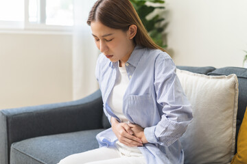 Sick asian young woman in pain, hand holding belly, stomach pain from food poisoning, girl hurt...