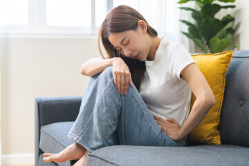 Sick asian young woman in pain, hand holding belly, stomach pain from food poisoning, girl hurt...