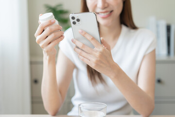 Health care asian young woman using smart phone for reading, searching prescription on bottle...