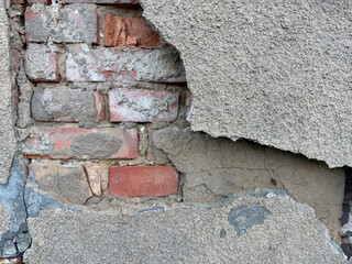 Old, cracked wall with large sections of plaster peeling away, revealing the red bricks underneath. The surface shows weathering, structural decay, and natural aging, creating a textured.