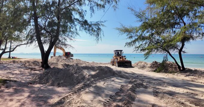 beachside construction scene: an excavator digs from a sand mound while a bulldozer clears a path. Trees frame the shore, and the ocean glistens under a sky.