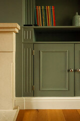 Obraz premium Green painted custom built in cabinet and bookshelf with small colorful books next to a decorative stone fireplace