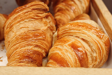 Golden brown croissants in a rustic wooden basket, offering a buttery flaky pastry for breakfast or brunch
