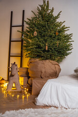 Cozy bedroom corner with large christmas tree wrapped in burlap decorated with tiny warm string lights wooden ornaments gift boxes and rocking horse for peaceful festive atmosphere