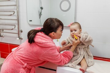 Mother brushing baby's teeth on washing machine. Baby care.