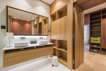 The bathroom features a wooden cabinet with sinks, a large mirror, and shelves. The light color...