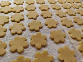 Batch of unbaked Linzer flower cookies. Many raw Linzer cookies in flower shapes on parchment paper.