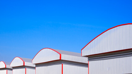 Row of rental warehouse industrial factory buildings group with dome roof and aluminum corrugated steel wall against blue sky background, perspective side view with copy space © Prapat