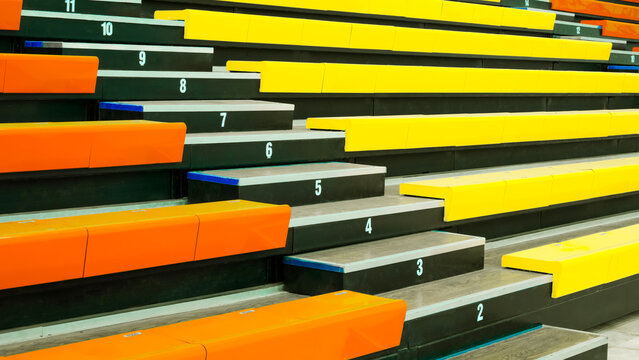 Rows of empty colorful orange and yellow stadium seats with white numbers. Indoor sports arena bleachers or grandstand background for spectators. perspective side view