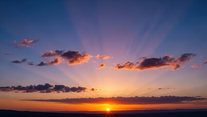 Bright orange sun shining with dramatic light rays through beautiful clouds in a colorful evening sky over dark hills