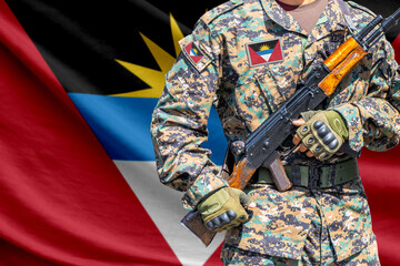 Obraz premium Antigua and Barbuda flag with soldier in military uniform holding assault rifle in front of it