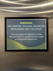 A sign warning message on wall of elevator stating no jumping, rocking, bouncing or running into the door
