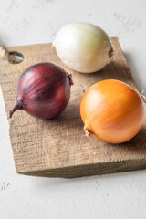 Three whole onions on rustic board showing red, yellow, and white varieties