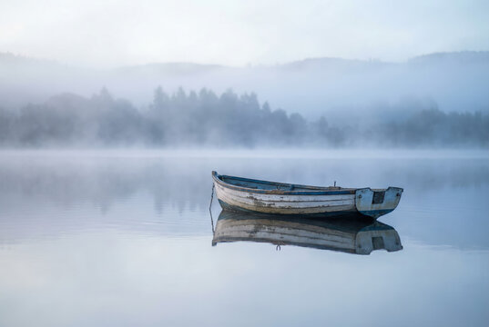 Serene Misty Morning on a Calm Lake with Isolated Rowboat Reflecting in Still Waters - Powered by Adobe