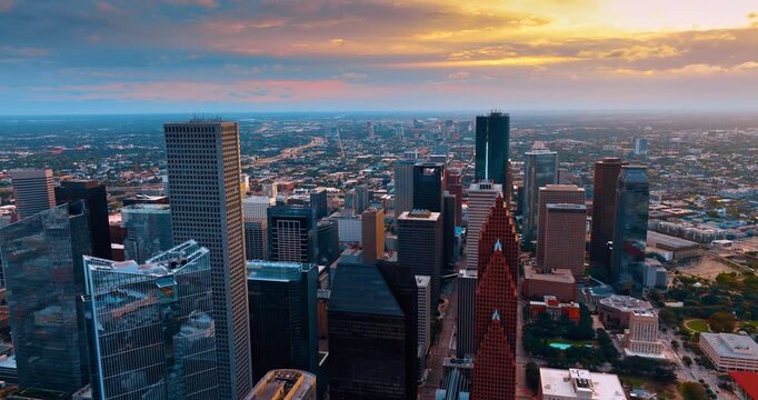 Footage over the tops of multiple diverse skyscrapers in the metropolis downtown. Breath-taking sky with clouds lit by setting sun at backdrop. Houston, Texas, USA.