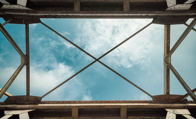Looking up through a sturdy metal framework at a serene blue sky adorned with soft clouds, symbolizing architectural strength and open possibilities for growth and innovation
