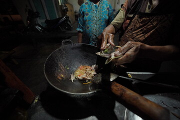 A person is cooking fish in a wok on a stove in an outdoor setting
