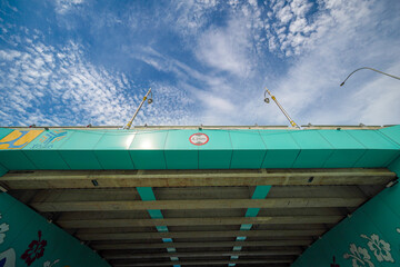 Vibrant Underpass Mural with Teal and Floral Accents, Illuminated by Streetlights Under a Dramatic Sky
