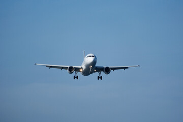 White Airplane Approaching for Landing Against Blue Sky and Clouds