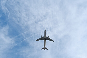 Fototapeta premium White Plane Overhead in Light Clouds. White Jet Soaring Overhead in Clear Blue Sky with Light Clouds
