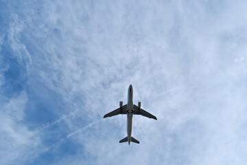 White Plane Overhead in Light Clouds. White Jet Soaring Overhead in Clear Blue Sky with Light Clouds
