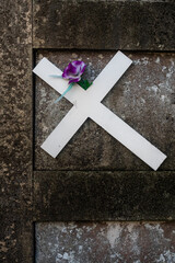 Una croce bianca di legno e un fiore viola appoggiati su una tomba del cimitero monumentale di San Michele a Venezia
