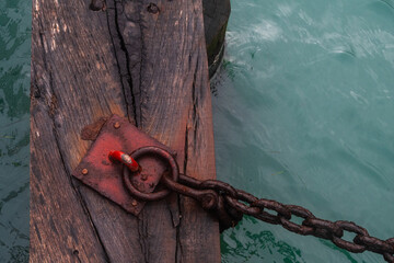 Dettaglio di una catena arrugginita fissata a un anello sul pontile di legno di un imbarcadero dei vaporetti a Venezia