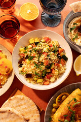 Moroccan couscous with vegetables, hummus, citrus salad and flatbread on a warm table