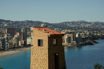 Ancient tower on the Mediterranean coast with modern architectural buildings in the background.