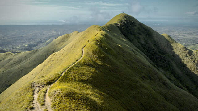 Aerial view of a winding path snaking across the verdant, sun-drenched peaks of Cerro Gaital, contrasting with the hazy horizon, El Valle de Ant&Atilde;&sup3;n, Cocl&Atilde;&copy; Province, Panama.