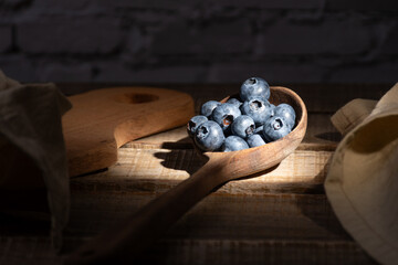Wooden ladle with blueberries illuminated by a ray of sunlight.