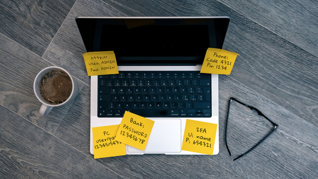 Unsecured Login Credentials and Private Pins Spread Across a Laptop Keyboard on Yellow Sticky Notes