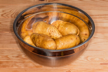 Raw washed yellow potato tubers in stainless steel kitchen bowl