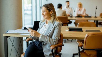 Woman in business attire smiles while using a smartphone in modern office setting