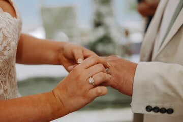 Bride placing a diamond wedding ring on the groom's finger during a marriage ceremony, symbolizing...