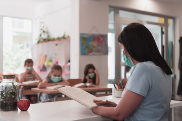 Multiracial group of kids wearing face masks working at class, writing and listening explanations of teacher in classroom