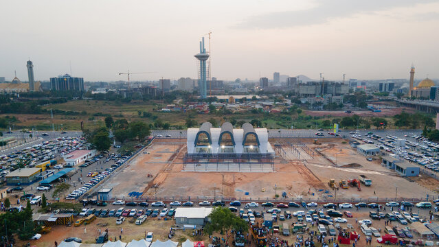 Aerial view of the National Ecumenical Centre's white arches contrasting against the earth tones and distant city skyline, Abuja, Federal Capital Territory, Nigeria.
