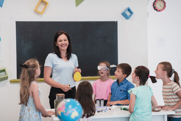 Elementary School Science Classroom: Enthusiastic Teacher Explains Chemistry to Diverse Group of Children, Little Boy Mixes Chemicals in Beakers. Children Learn with Interest