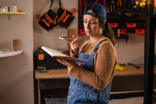 Portrait of female repairman or mechanic wearing overalls, craftsman dictate voice message on smartphone in garage workshop - Powered by Adobe