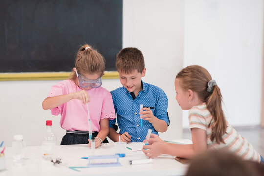 Elementary School Science Classroom: Enthusiastic Teacher Explains Chemistry to Diverse Group of Children, Little Boy Mixes Chemicals in Beakers. Children Learn with Interest - Powered by Adobe
