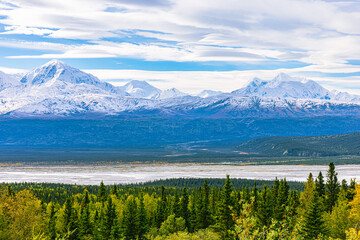 Panoramic view of Alaska wilderness featuring snow-covered mountains, vast plains, and dense evergreen forest.