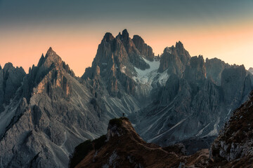 Obraz premium Alpine landscape of Cadini di Misurina with rugged mountain peak and male tourist hiking during sunset in Dolomites, Italy