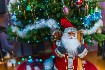 Close up view of Santa doll with skis stands near decorated Christmas tree with lights creating festive home mood. Sweden.