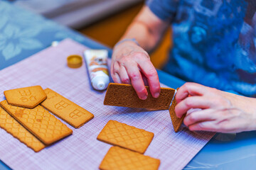Female hands assembling gingerbread house pieces with baking glue during festive Christmas preparation. Sweden.
