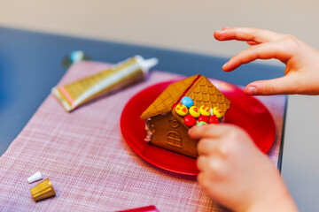 Close up view of child decorating gingerbread house with colorful candy during warm Christmas crafting moment. Sweden.
